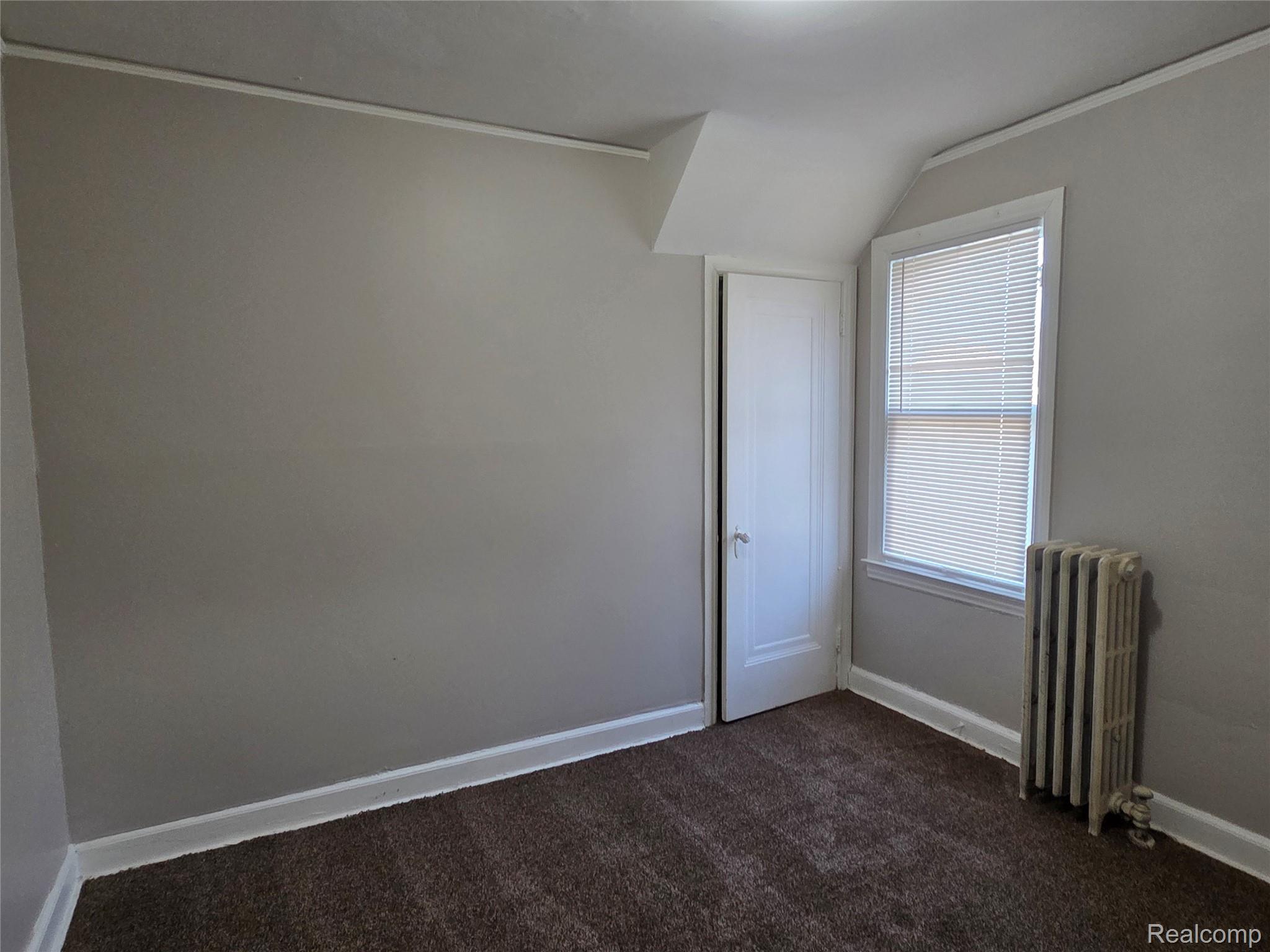 5274 Nottingham Road Detroit, MI 48224 - Photo 8 of 22 Unfurnished room featuring radiator, dark carpet, crown molding, and lofted ceiling