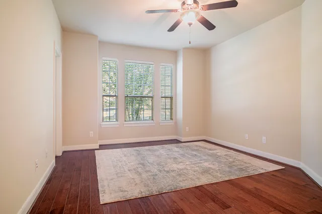 an empty room with wooden floor chandelier fan and windows
