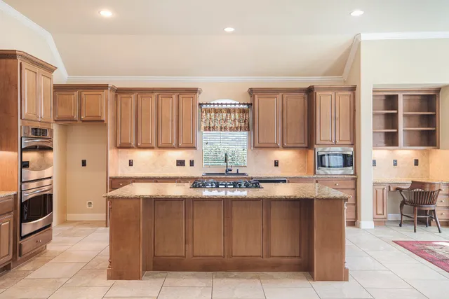 a kitchen with kitchen island granite countertop a stove top oven a sink dishwasher and cabinets with wooden floor