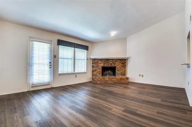 an empty room with wooden floor fireplace and windows