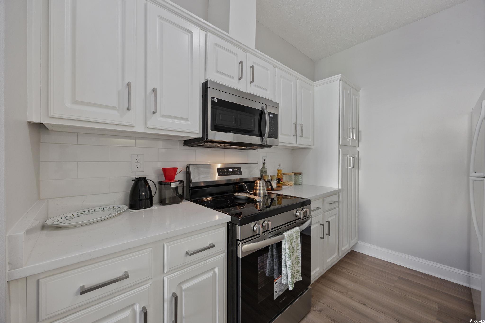 111 Fountain Pointe Lane, Unit 104 Myrtle Beach, SC 29579 - Photo 5 of 30 Kitchen featuring appliances with stainless steel finishes, white cabinetry, tasteful backsplash, and light wood finished floors