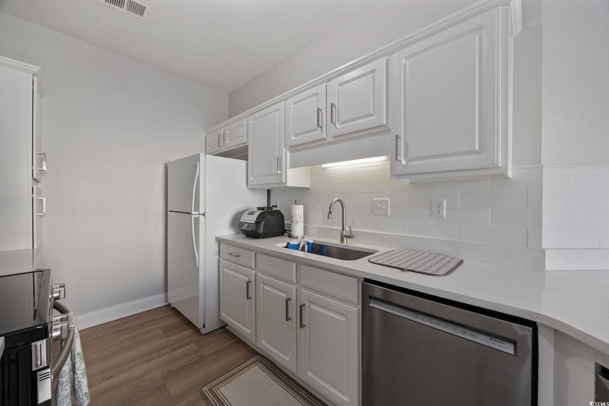 111 Fountain Pointe Lane, Unit 104 Myrtle Beach, SC 29579 - Photo 6 of 30 Kitchen with white cabinets, appliances with stainless steel finishes, dark wood-style floors, backsplash, and light stone countertops