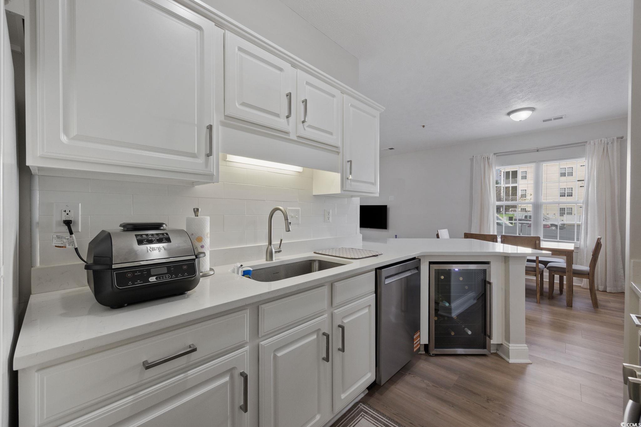 111 Fountain Pointe Lane, Unit 104 Myrtle Beach, SC 29579 - Photo 7 of 30 Kitchen featuring white cabinets, wine cooler, decorative backsplash, stainless steel dishwasher, and a peninsula