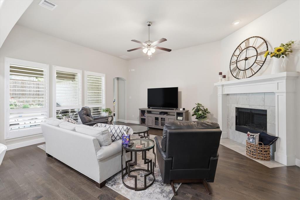 9708 Surveyor Road Oak Point, TX 75068 - Photo 12 of 34 Spacious living area featuring wood-finish flooring, a white mantel fireplace with tile surround, and three windows with plantation shutters