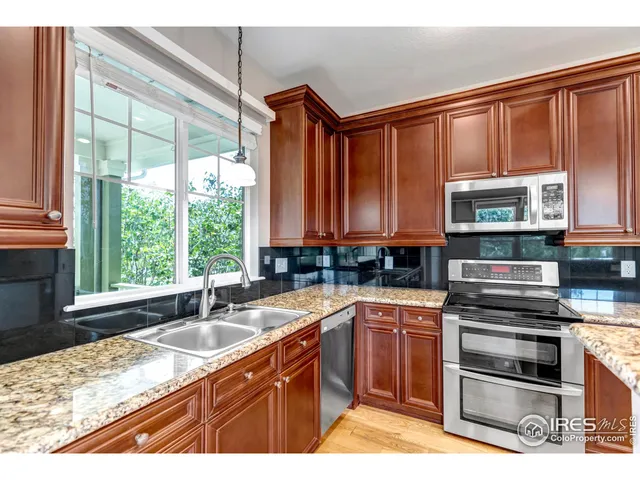 a kitchen with stainless steel appliances granite countertop a stove top oven a refrigerator a dining table and chairs with wooden floor