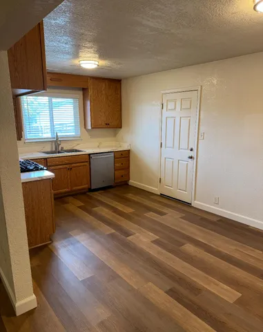 a large kitchen with granite countertop a stove a sink a refrigerator and white cabinets with wooden floor