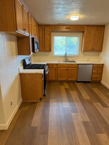 a large kitchen with stainless steel appliances a large counter top a stove and a wooden floors