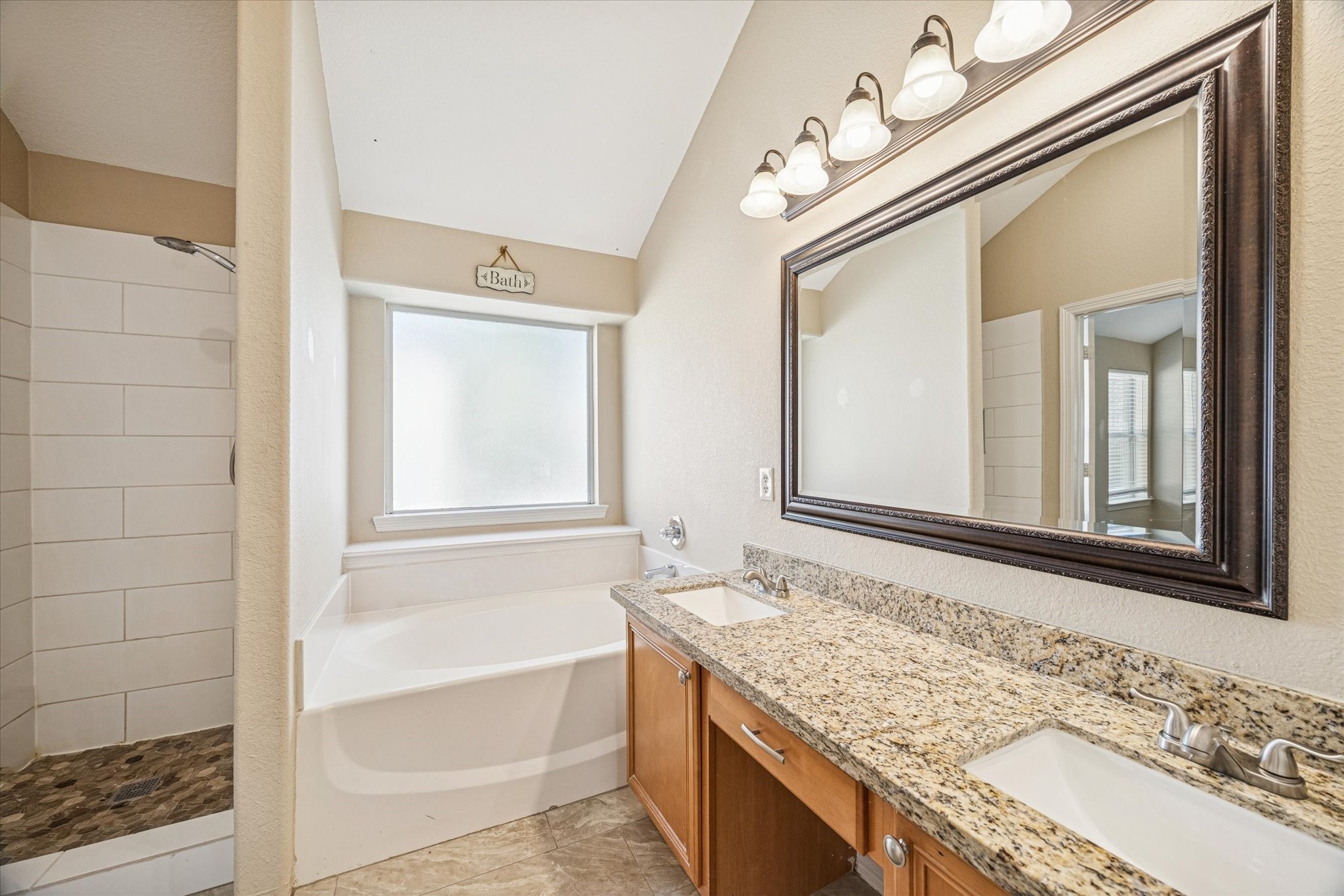 19034 Ranchcrest Drive Magnolia, TX 77355 - Photo 11 of 26 This primary bathroom features a stylish design with a large mirror above a double-sink vanity with granite countertops. It includes a spacious bathtub and a separate walk-in shower with tiled flooring, offering both functionality and elegance.