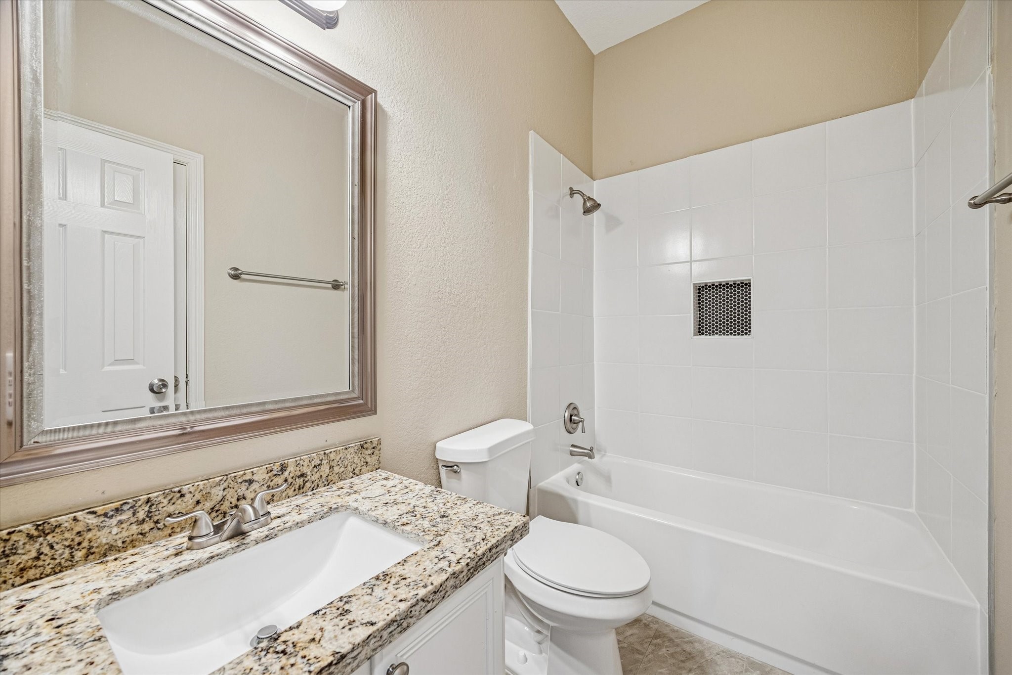19034 Ranchcrest Drive Magnolia, TX 77355 - Photo 20 of 26 This bathroom features a modern design with a granite countertop, undermount sink, large framed mirror, and a white tiled shower-tub combo. The neutral walls and fixtures create a clean, inviting space.