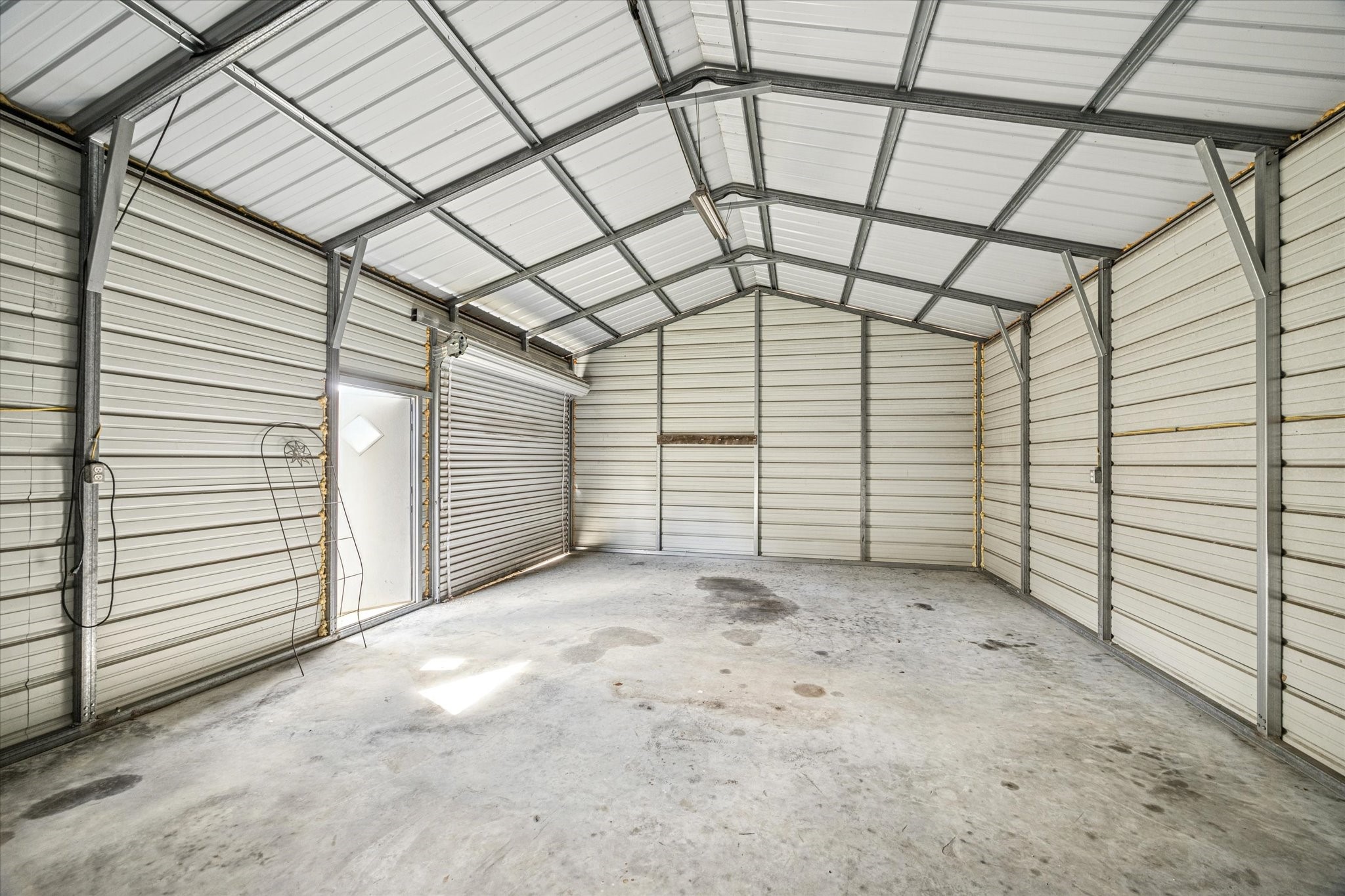 19034 Ranchcrest Drive Magnolia, TX 77355 - Photo 22 of 26 This spacious metal storage features a high ceiling, durable concrete flooring, and ample room for storage or parking. It includes a roll-up door for easy access and a side entrance for convenience. Ideal for vehicles, workshop use, or additional storage space.