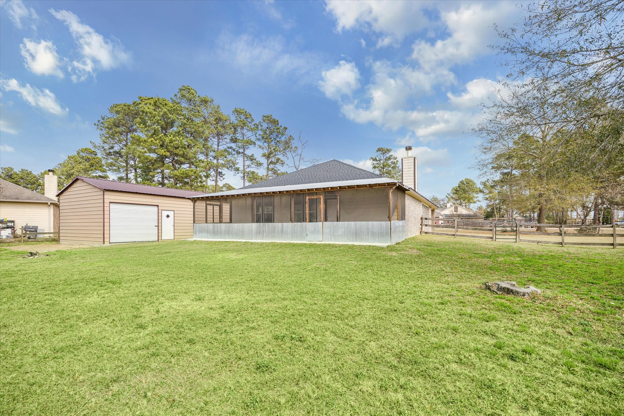 19034 Ranchcrest Drive Magnolia, TX 77355 - Photo 24 of 26 This photo shows a backyard with a well-maintained lawn, a screened patio, and a detached garage. The area is spacious, surrounded by trees and a wooden fence, offering a private and serene outdoor space.