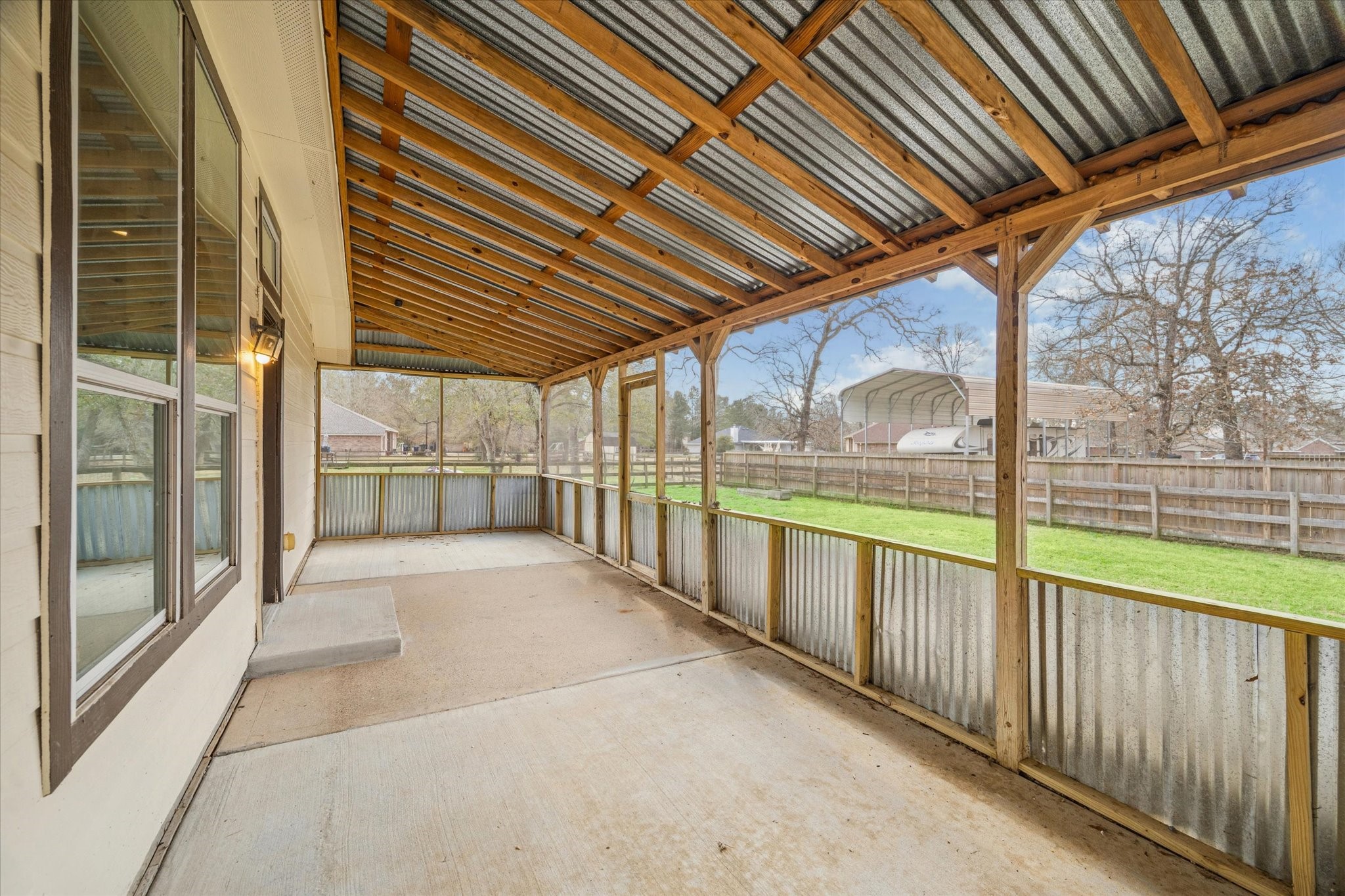 19034 Ranchcrest Drive Magnolia, TX 77355 - Photo 25 of 26 This spacious covered patio with a corrugated metal roof and wooden supports, perfect for outdoor gatherings. It overlooks a fenced backyard with green grass, offering a private and cozy outdoor space.