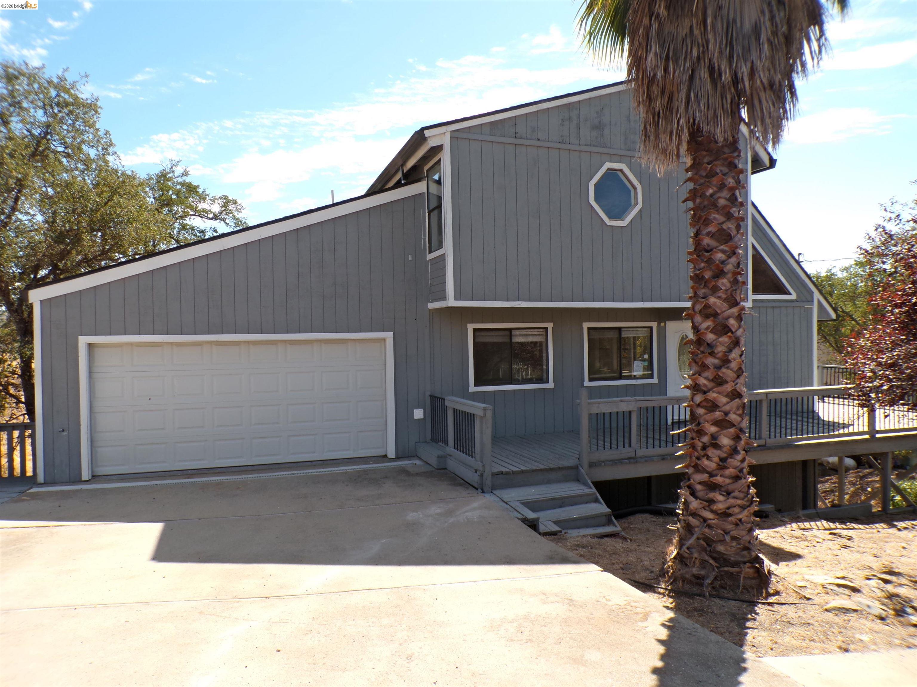 Gray exterior with contrasting white trim, featuring a two-car garage, an octagonal window, and an expansive wooden deck