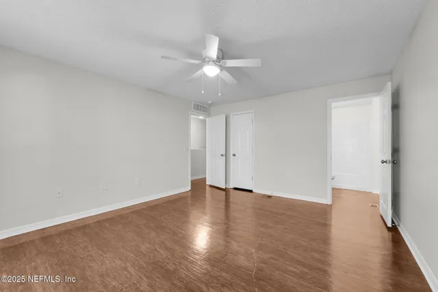 an empty room with wooden floor ceiling fan and window