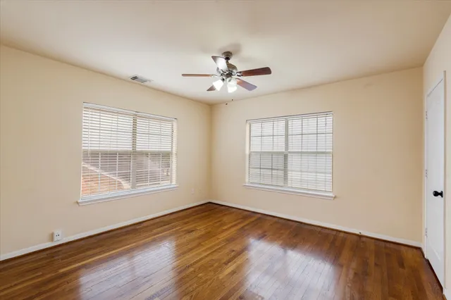 an empty room with wooden floor ceiling fan and windows