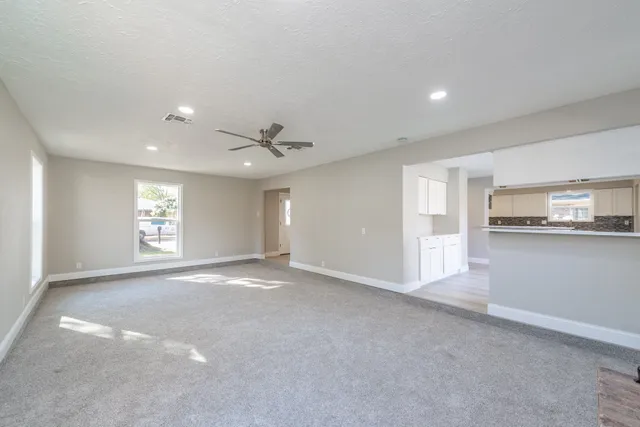 a view of an empty room with kitchen and window