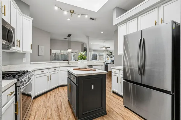 a kitchen with stainless steel appliances granite countertop a refrigerator a sink a stove and white cabinets with wooden floor