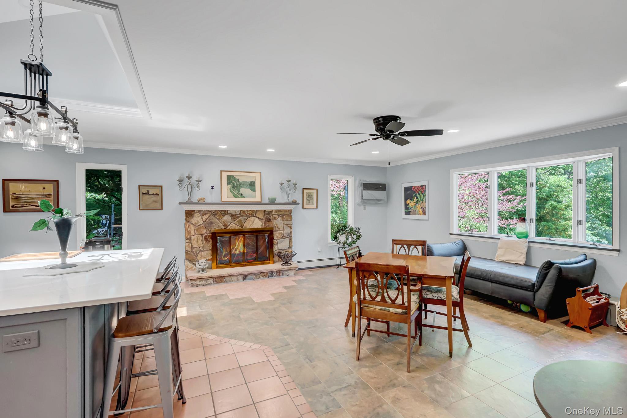 100 Elwood Road Northport, NY 11768 - Photo 9 of 39 Spacious interior featuring a stone fireplace with a hearth, a kitchen island with a light-toned countertop, a multi-pane window configuration, recessed lighting, and a ceiling fan