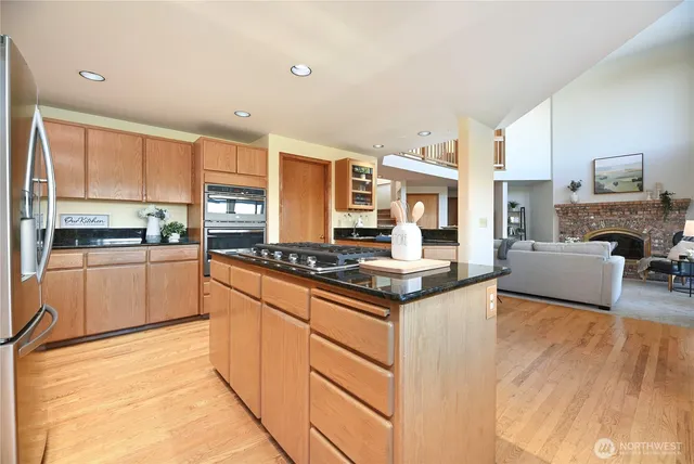 a kitchen with stainless steel appliances granite countertop a stove top oven a sink dishwasher and a refrigerator with wooden floor