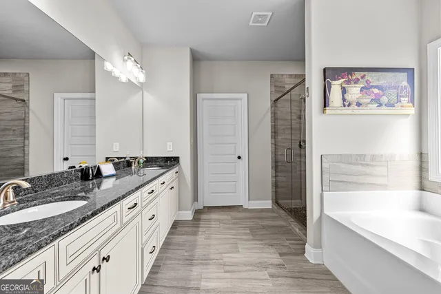 a bathroom with a granite countertop double vanity sink a mirror a bathtub and shower