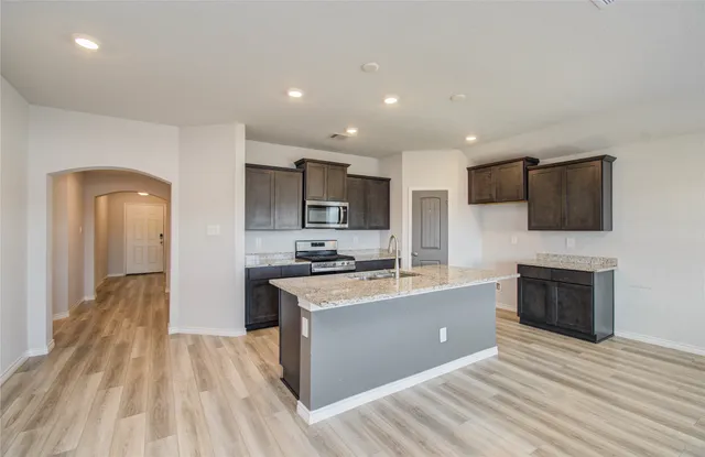 a large kitchen with stainless steel appliances granite countertop a stove top oven a sink dishwasher a refrigerator and a fireplace with wooden floor