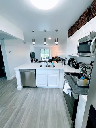 a kitchen with stainless steel appliances a sink a stove top oven a chimney wooden floor and cabinets