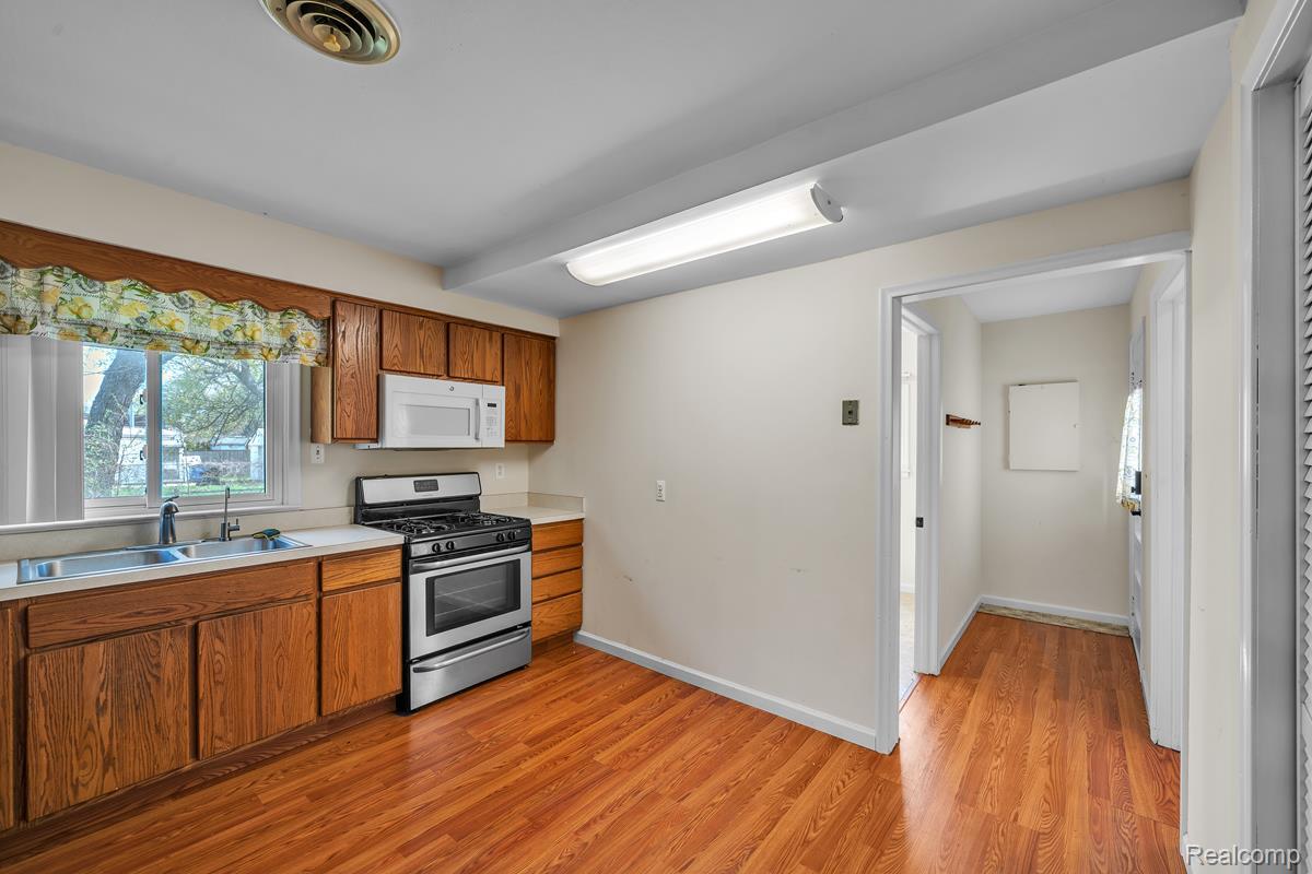 8620 Stephens Road Warren, MI 48089 - Photo 8 of 15 Kitchen with stainless steel gas range oven, light countertops, wood finish cabinets, white microwave, and light wood-style floors