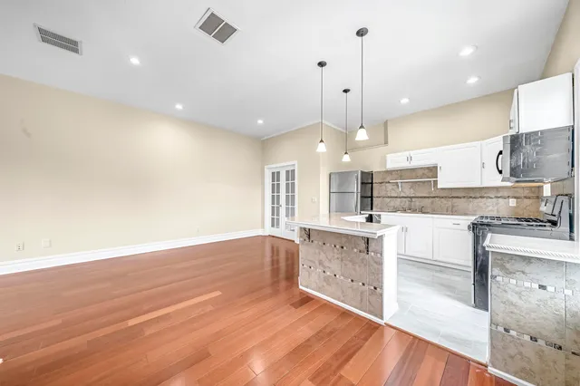 a large kitchen with granite countertop a stove a sink and white cabinets with wooden floor