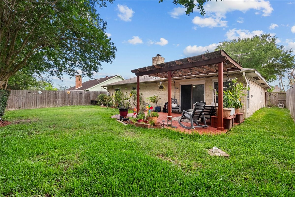 883 Silverpines Road Houston, TX 77062 - Photo 28 of 38 This photo showcases a spacious backyard with lush green grass and a wooden pergola over a patio area, perfect for outdoor seating and relaxation. The yard is fenced, providing privacy and a cozy atmosphere for entertaining or enjoying nature.