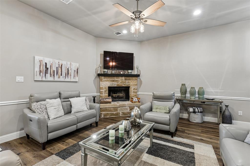 108 Maverick Lane Pilot Point, TX 76258 - Photo 5 of 27 Living area featuring wood-finish flooring, a stone-clad fireplace with a dark mantel, crown molding, and a ceiling fan with integrated lighting