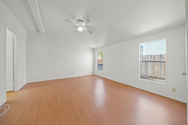 a view of an empty room with chandelier fan and wooden floor