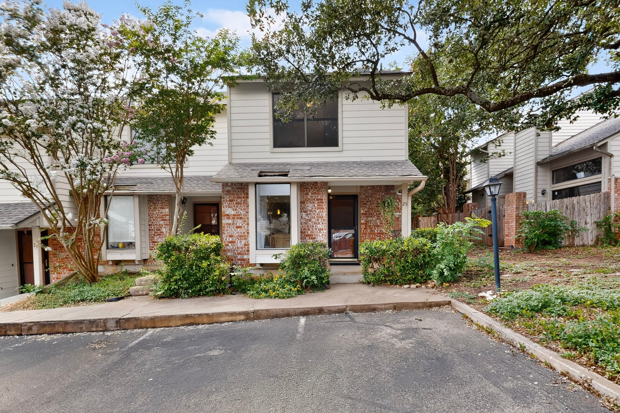 3801 Menchaca Road, Unit 25 Austin, TX 78704 - Photo 2 of 27 A charming townhouse with a blend of brick and siding, framed by mature trees and lush landscaping.
