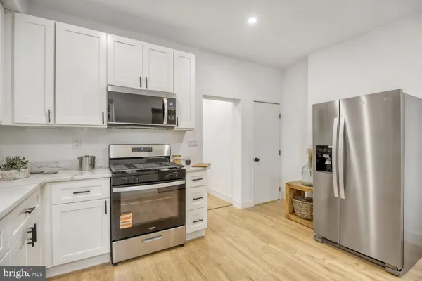 a kitchen with stainless steel appliances granite countertop a stove top oven a sink a refrigerator with white cabinets and wooden floor