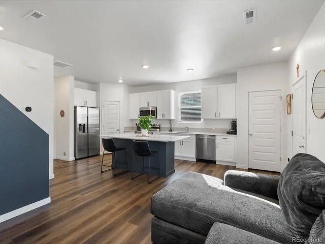 a kitchen with stainless steel appliances kitchen island granite countertop a refrigerator a sink a stove and white cabinets with wooden floor