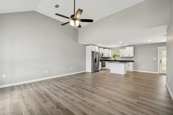 a view of an empty room with wooden floor and a ceiling fan