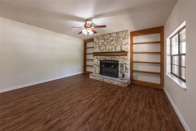 a view of an empty room with wooden floor fireplace and a window