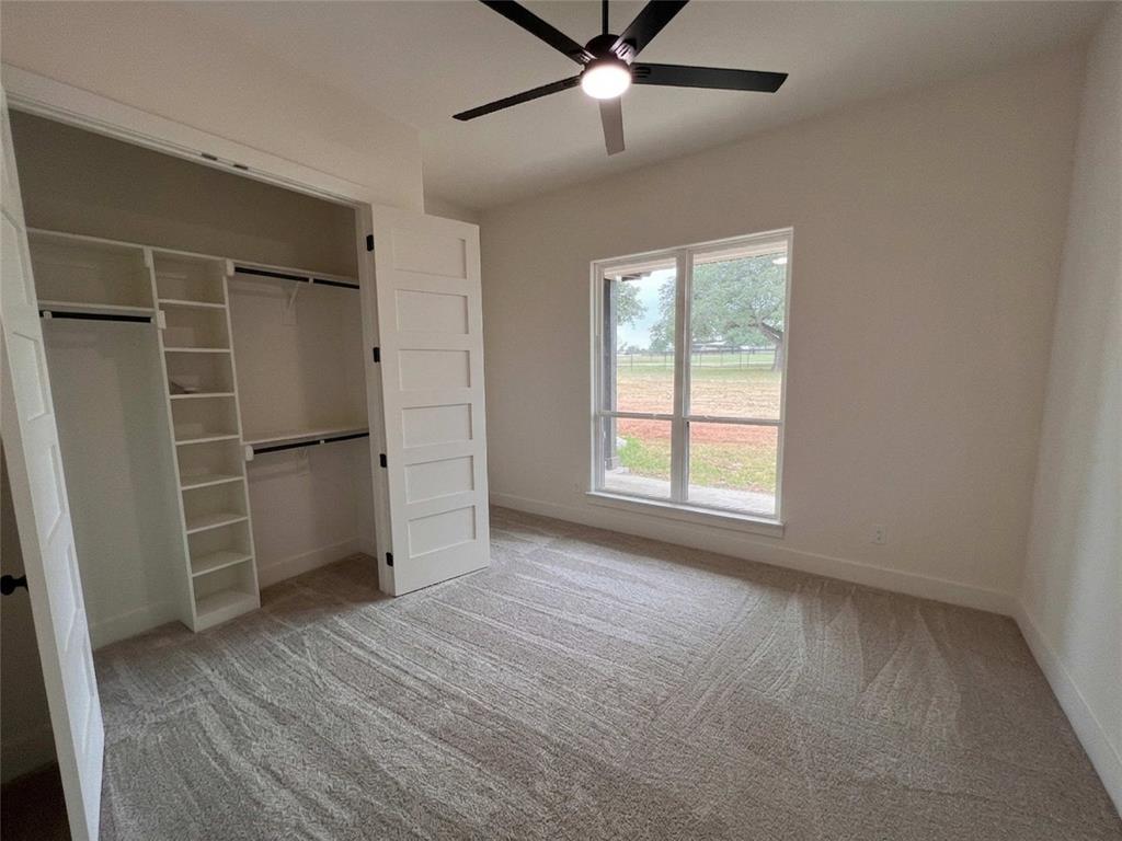 121 Cartwright Park Road Weatherford, TX 76087 - Photo 14 of 17 Interior room with light tan patterned carpet flooring, a window with exterior views, and a closet with a built-in shelving system
