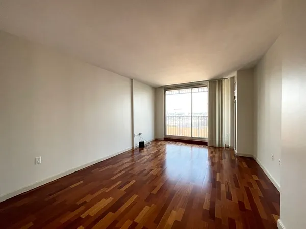 a view of an empty room with wooden floor and window