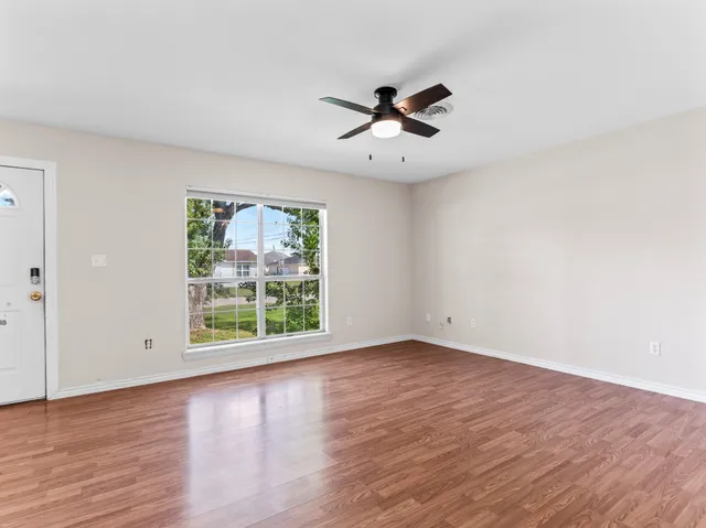an empty room with wooden floor fan and windows