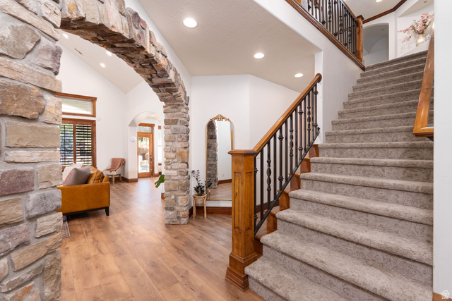 687 South 2080th Street East Springville, UT 84663 - Photo 11 of 149 Foyer featuring a stone archway, wood-finish flooring, a carpeted staircase with wood and wrought iron railing, vaulted ceilings, and recessed lighting