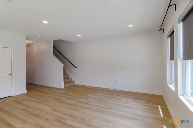 a view of an empty room with wooden floor and stairs
