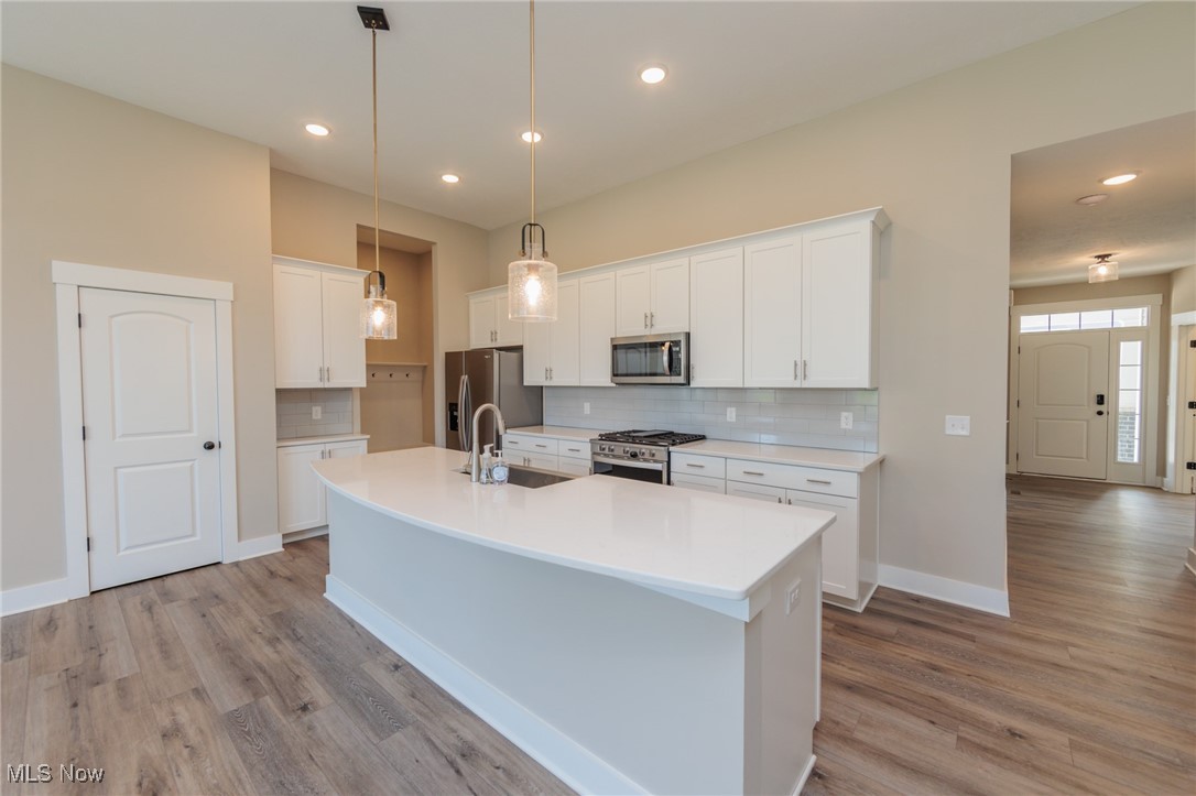 36458 Appian Way North Ridgeville, OH 44039 - Photo 15 of 37 Kitchen with light hardwood / wood-style flooring, decorative light fixtures, stainless steel appliances, white cabinetry, and a center island with sink