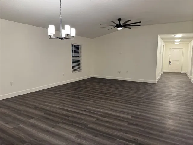 an empty room with wooden floor chandelier fan and windows