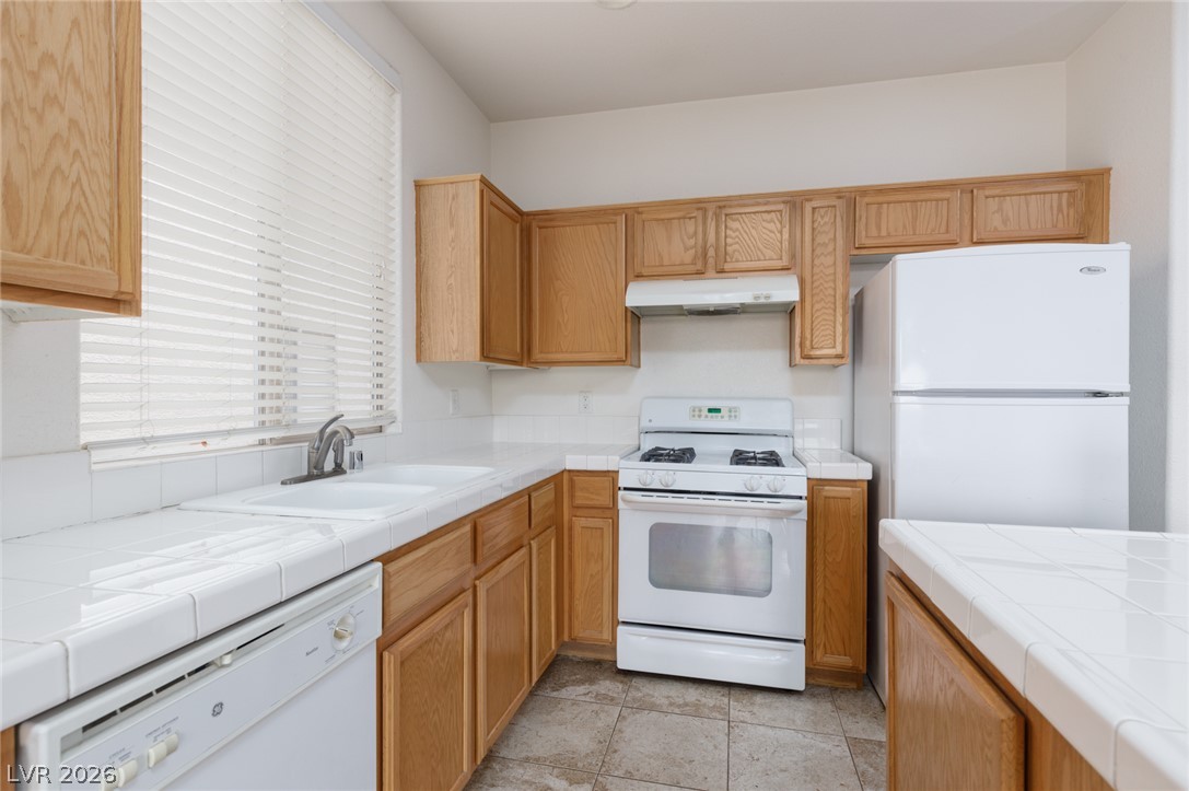 787 Rise Canyon Drive Henderson, NV 89052 - Photo 6 of 22 A compact kitchen with light wood cabinetry and white tiled countertops provides practical culinary space.