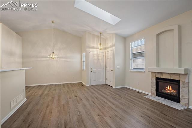 Unfurnished living room featuring lofted ceiling, plenty of natural light, wood finished floors, a skylight, and a fireplace