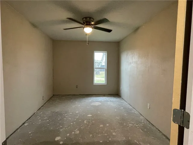 an empty room with a chandelier fan and windows
