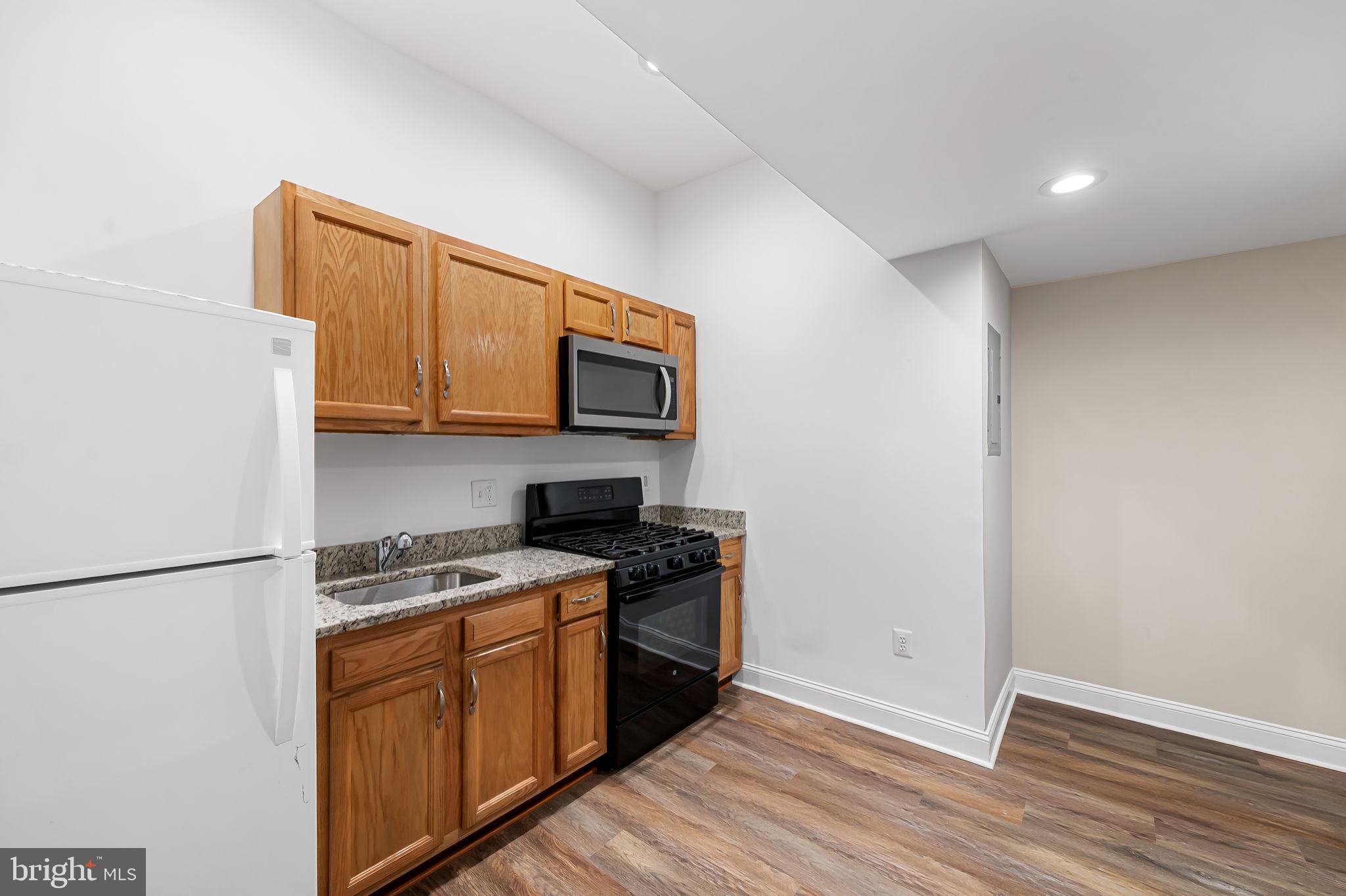 1005 Edmondson Avenue Baltimore, MD 21223 - Photo 21 of 45 a kitchen with stainless steel appliances granite countertop a stove top oven a sink a refrigerator with white cabinets and wooden floor