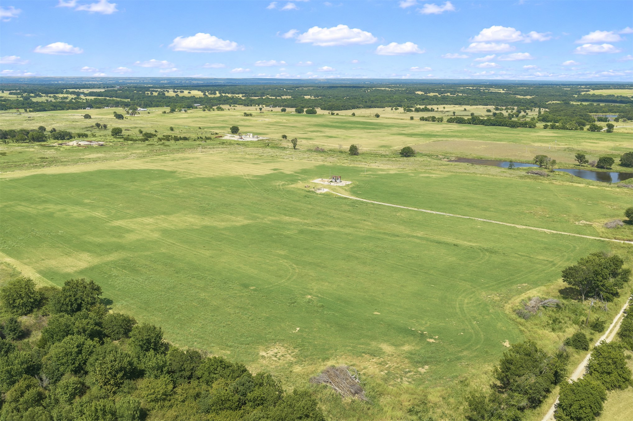 4 Keller Road Wilson, OK 73463 - Photo 7 of 32 Expansive green fields featuring mature trees, a natural pond, and an unpaved access road