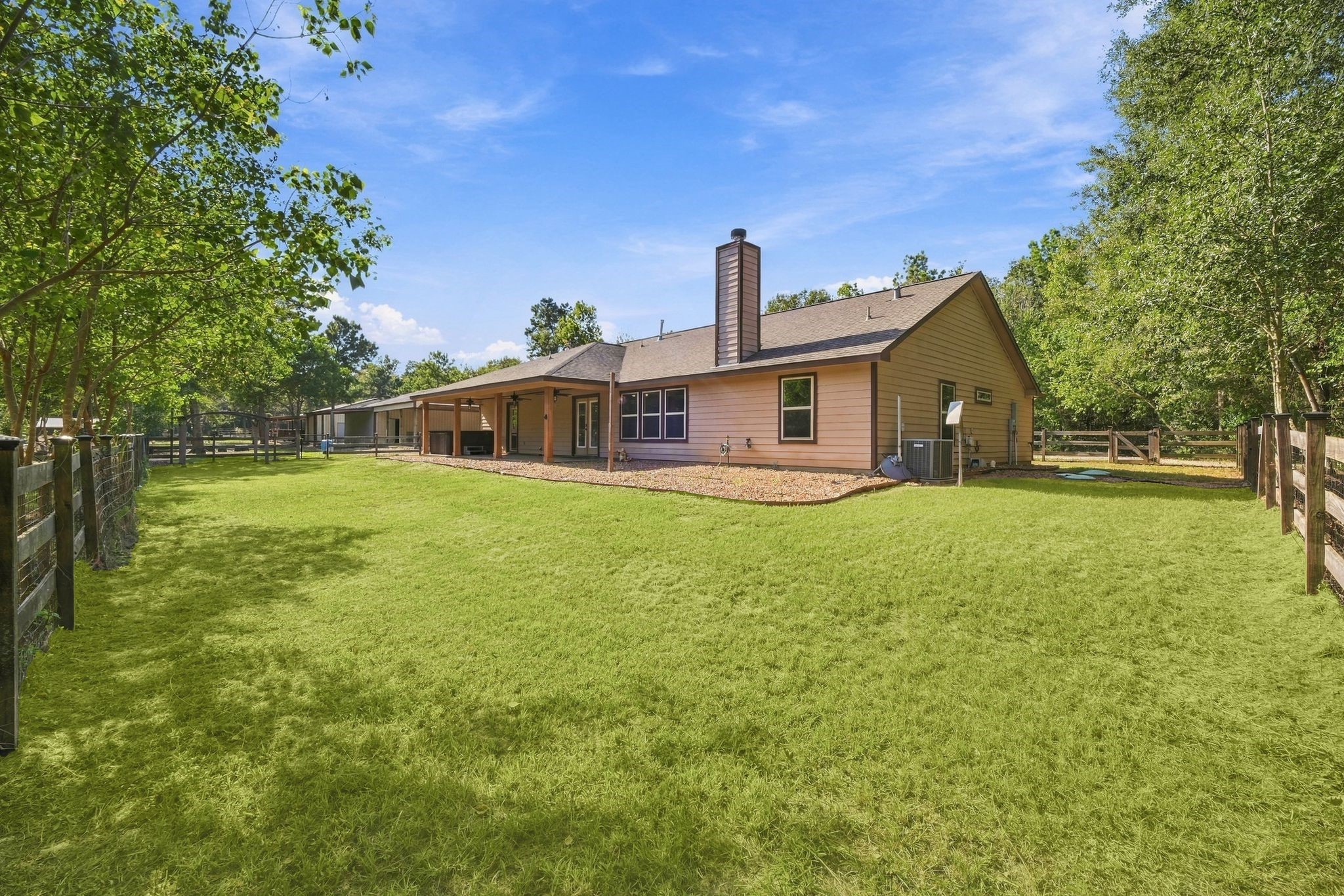 7049 Pine Shadows Road Cleveland, TX 77328 - Photo 30 of 49 Charming ranch-style home with a spacious backyard, surrounded by lush greenery and featuring a cozy patio area perfect for outdoor relaxation.