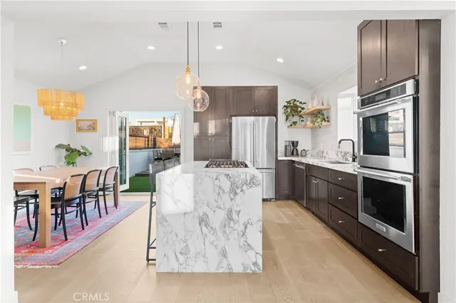 a large kitchen with stainless steel appliances kitchen island granite countertop a refrigerator a stove a sink a dining table and chairs with wooden floor